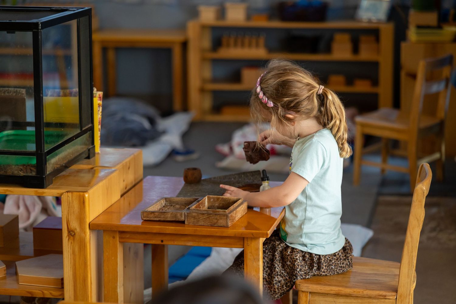 Montessori classroom with wooden tables and chairs displays hands-on learning activities and educational materials.