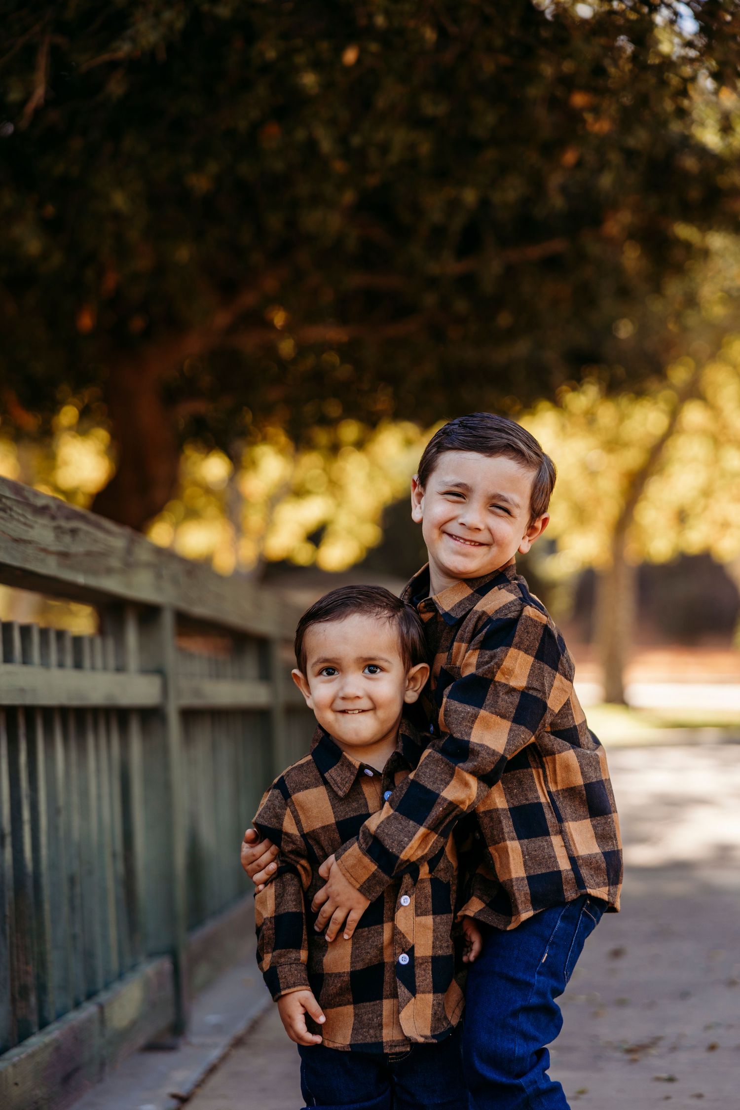 Children in matching plaid shirts share a sweet moment by wooden fence.