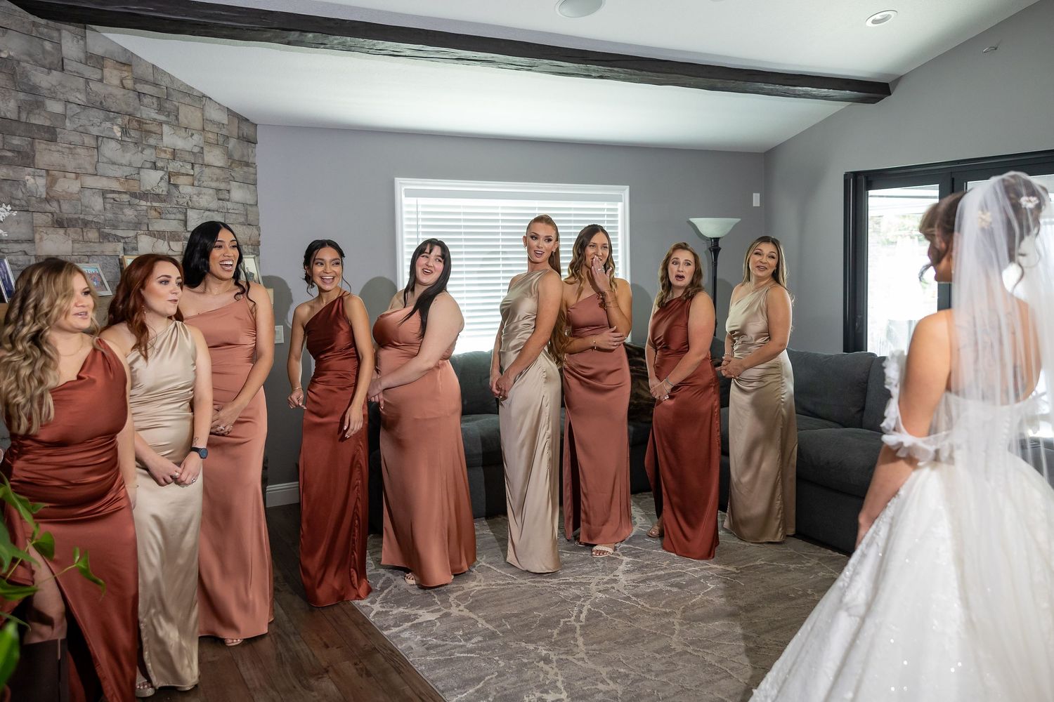 Bridesmaids in coral dresses react with excitement to seeing the bride in her wedding gown.