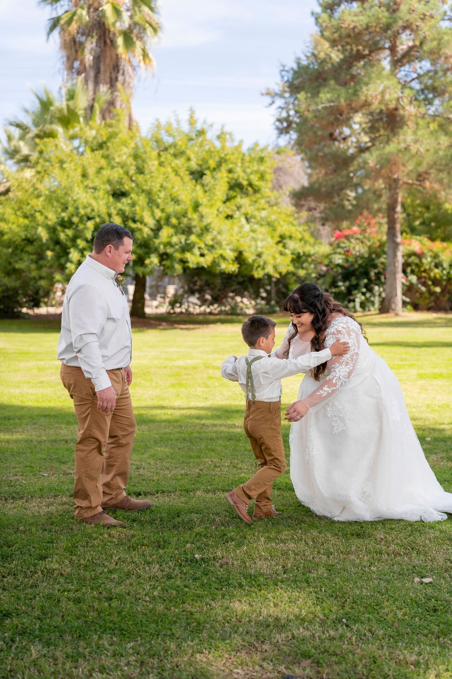 Playful outdoor wedding moment captured on a grassy lawn with palm trees in the background.