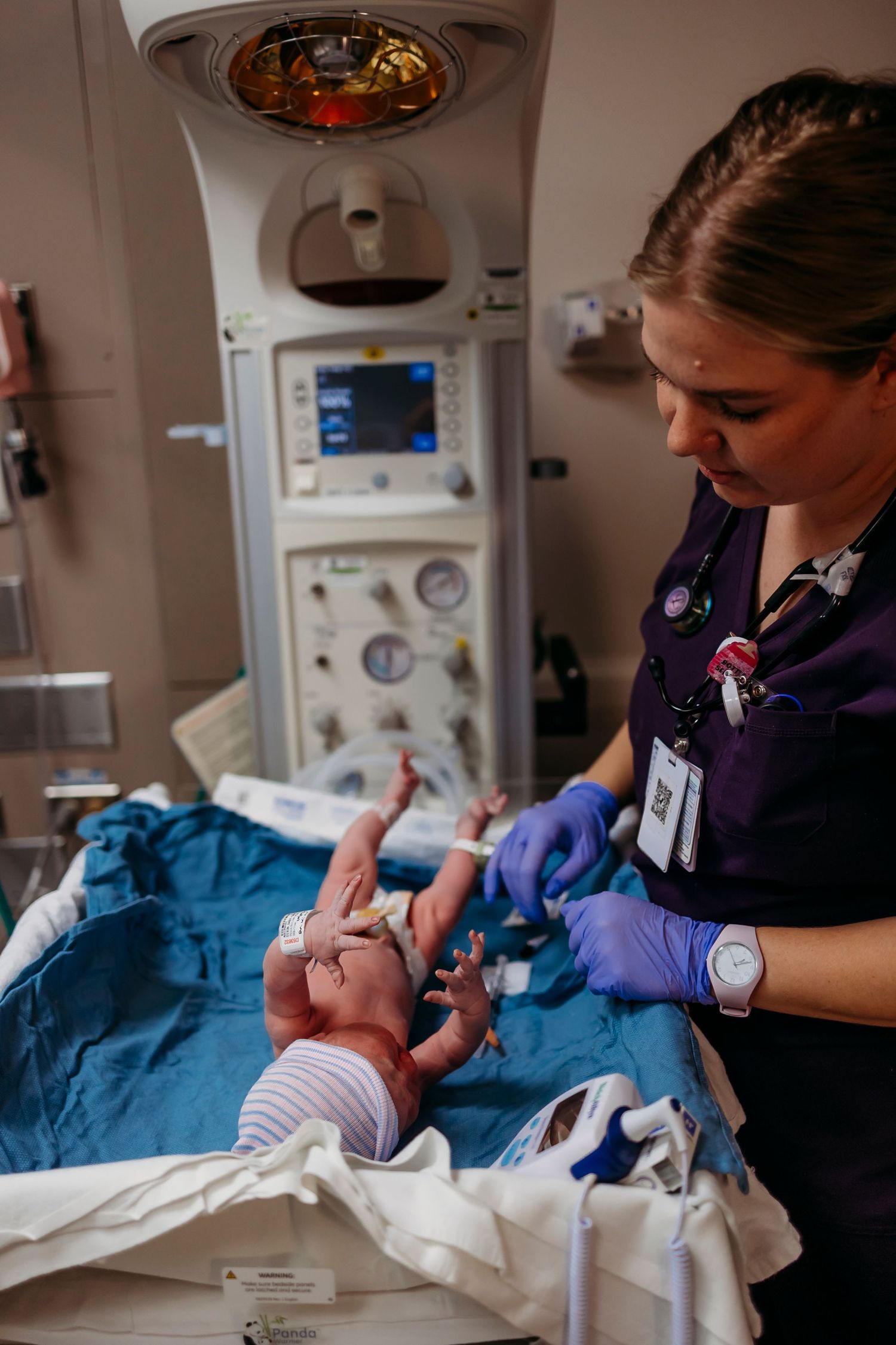 Healthcare worker tending to newborn baby under medical equipment.