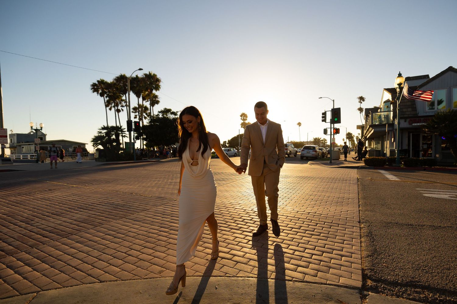 Silhouettes of people walking on a paved pathway during golden hour near the beach.