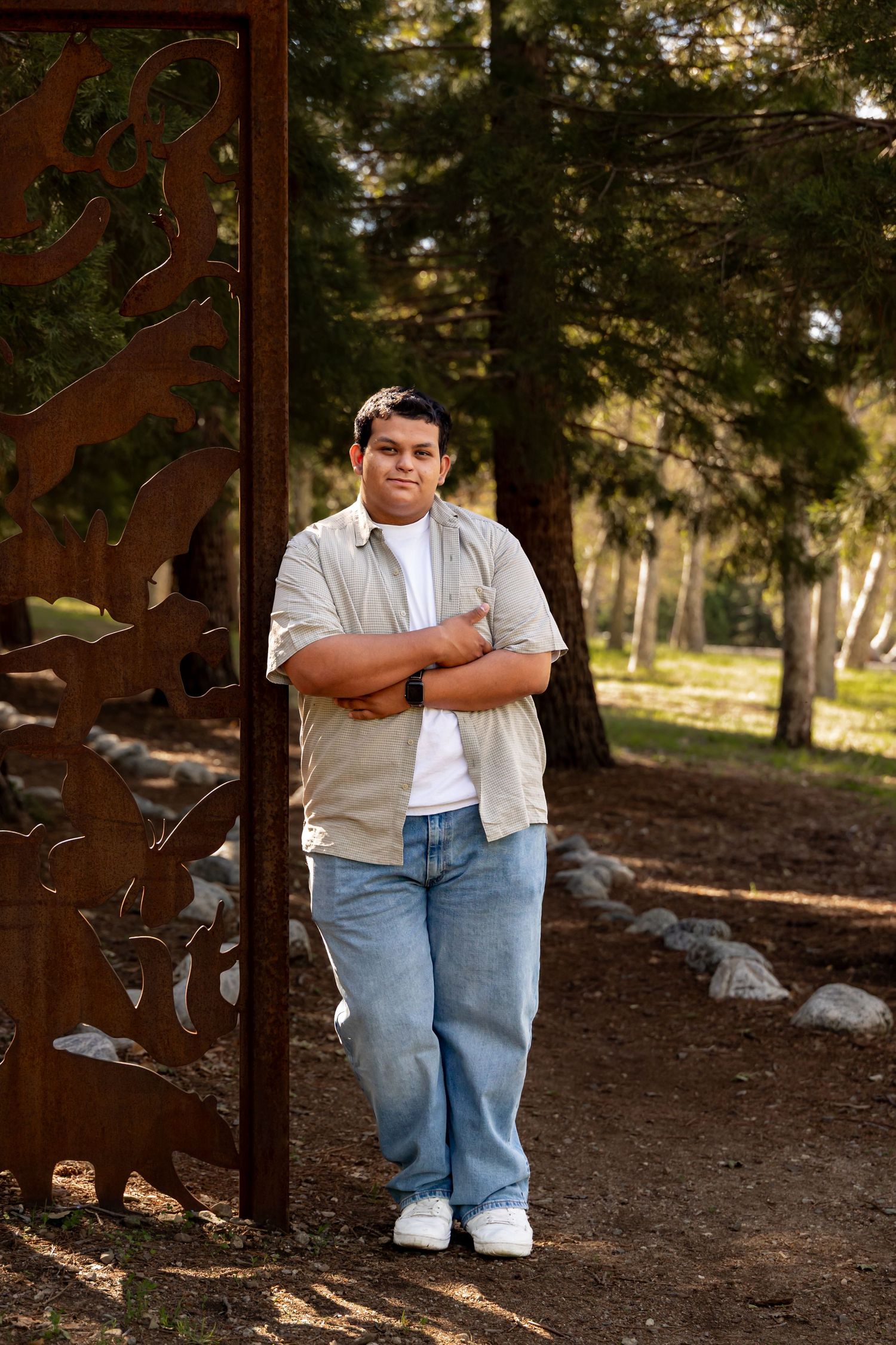 Someone poses confidently against a decorative metal gate in a wooded outdoor setting in Yucaipa.