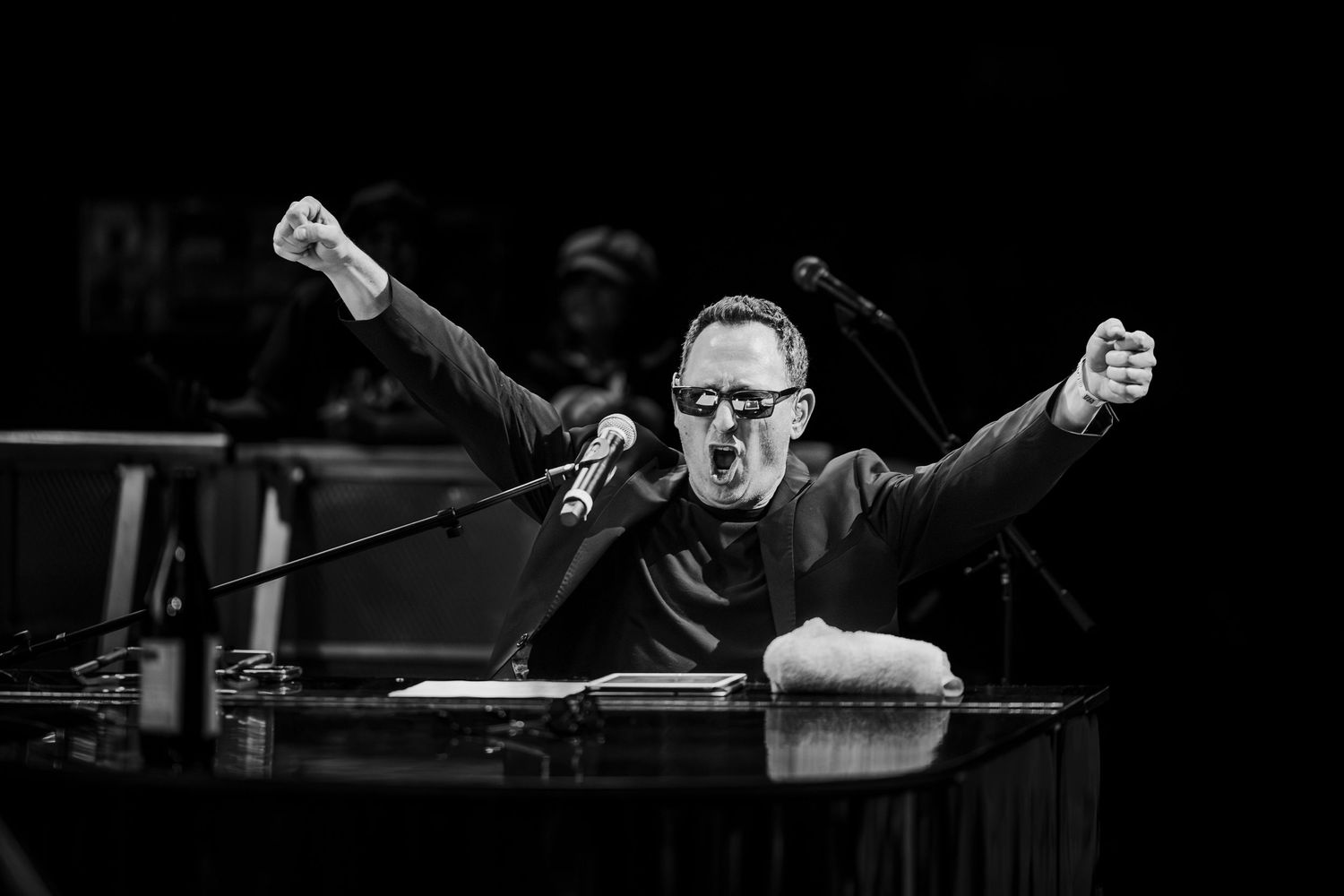 Black and white photo of performer with raised fists behind piano during emotional performance in Garden Grove.