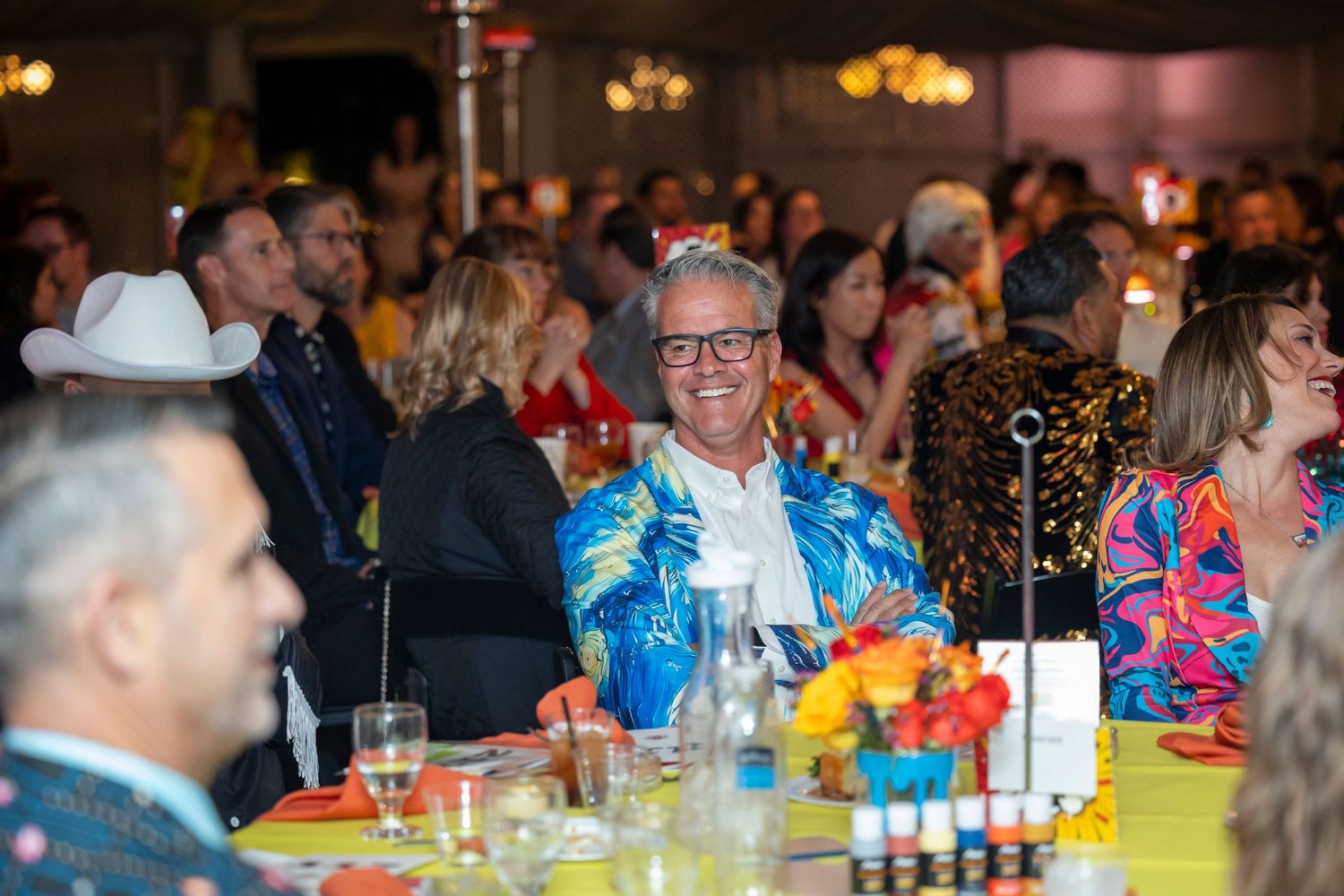 Event guests socializing at decorated round tables with warm ambient lighting.