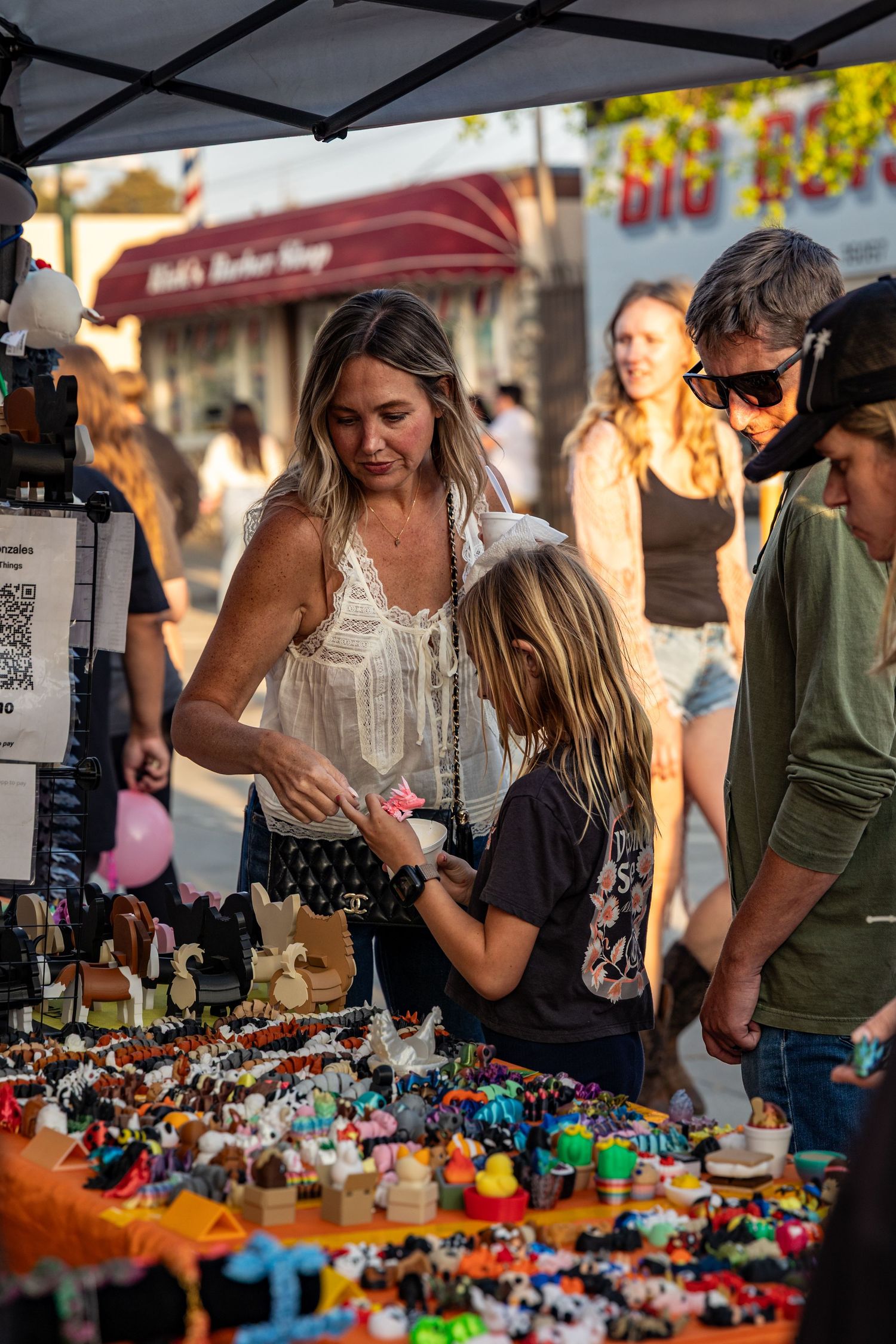 A vendor displays colorful merchandise at an outdoor market stall while customers browse.