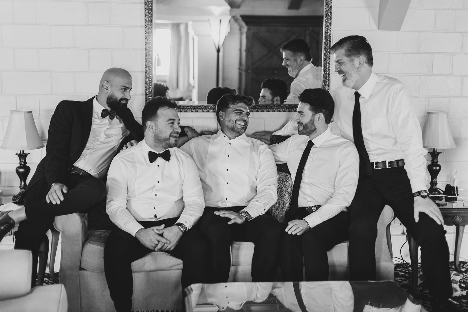 Black and white candid moment of groomsmen laughing together on couch.