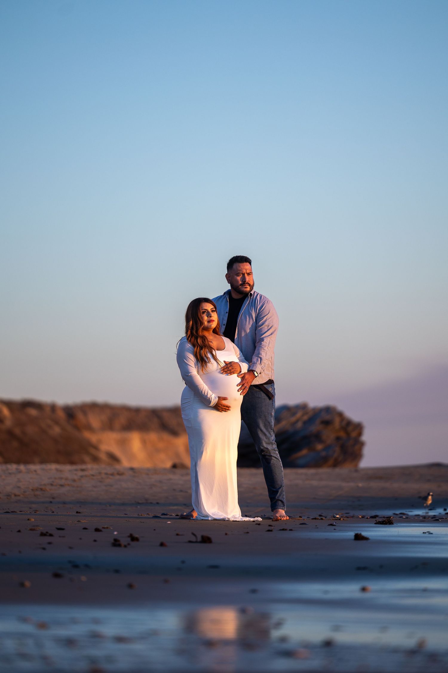 A romantic beach engagement session at sunset with cliffs and reflective water.