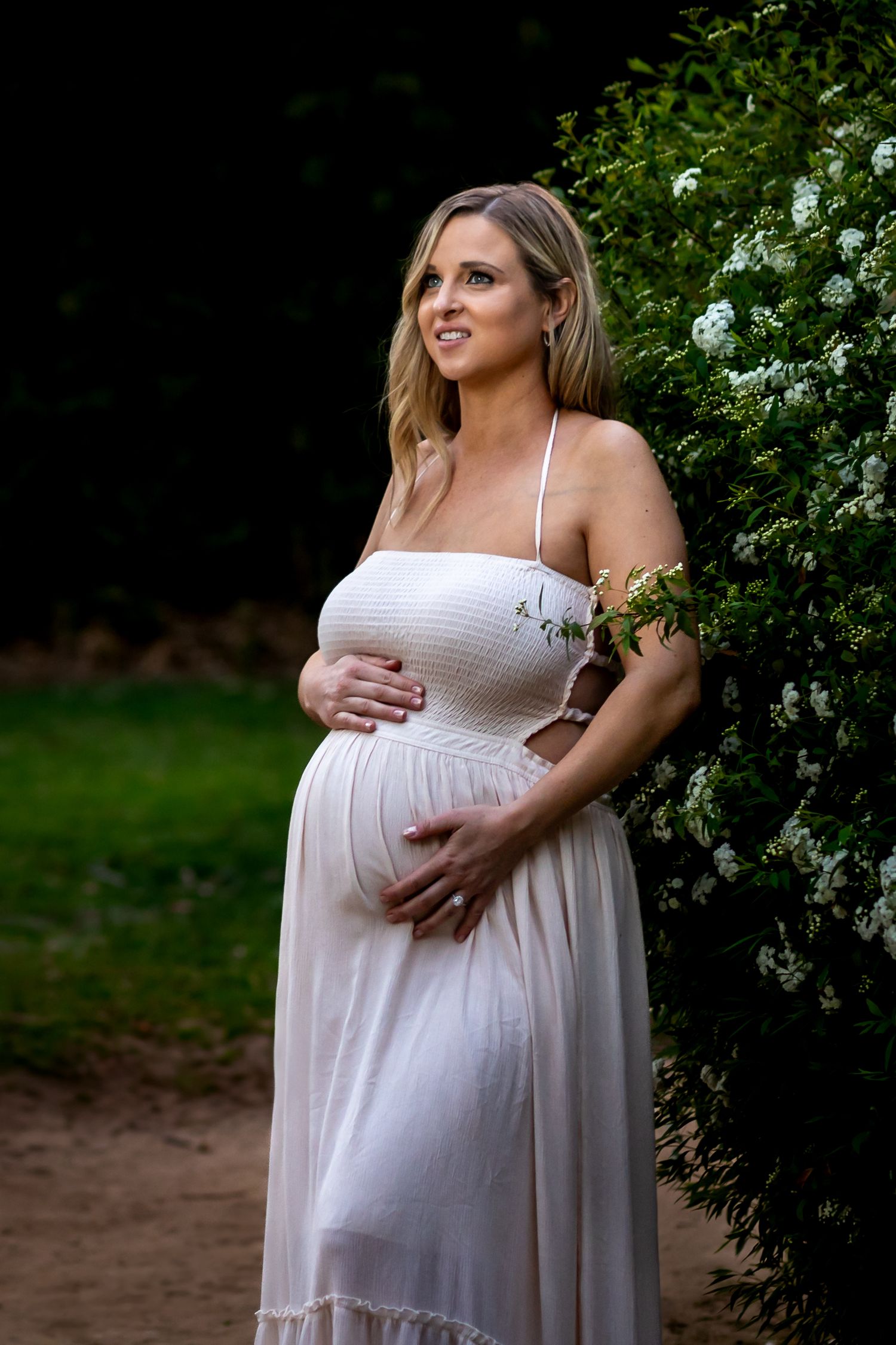 A serene maternity portrait against blooming white flowers in a garden setting.
