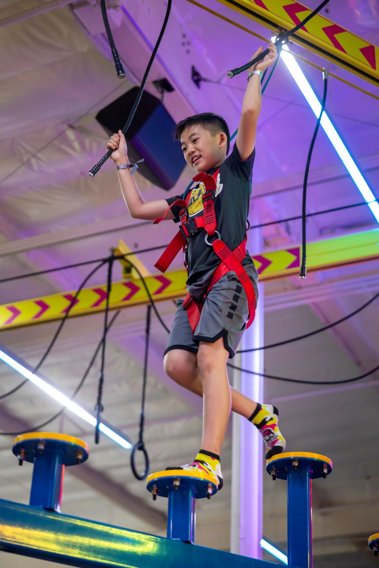 Child swinging and playing on colorful indoor climbing equipment with neon lighting.