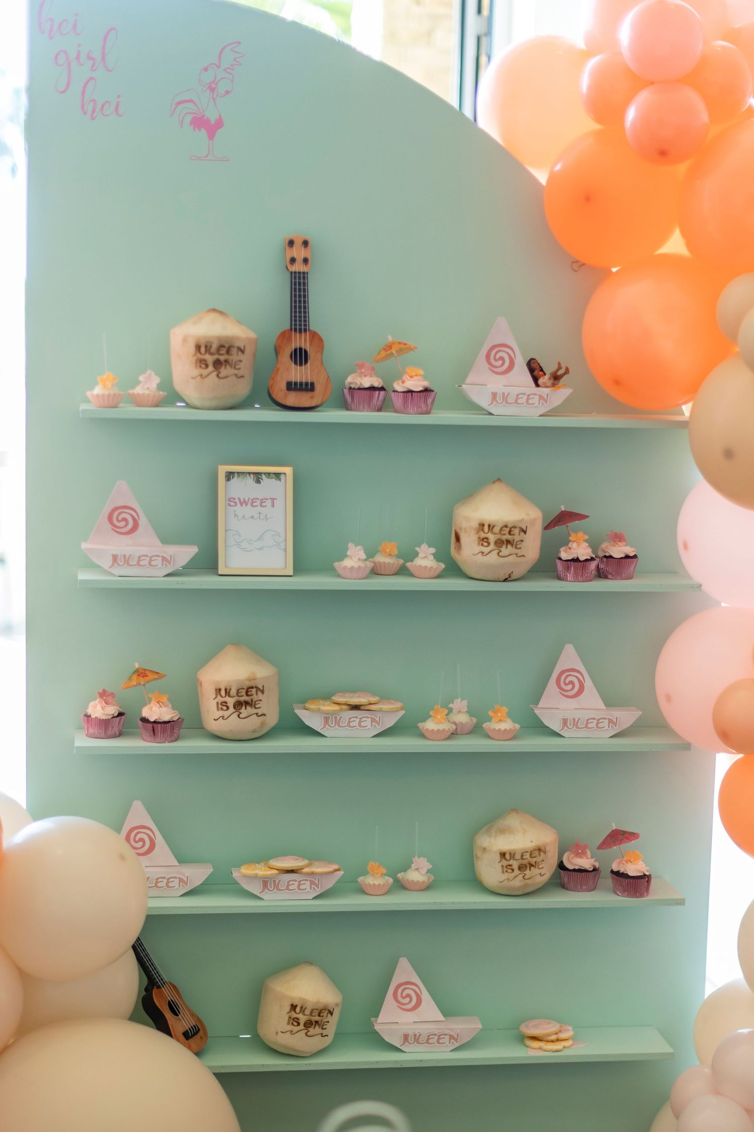 Mint green shelves display cupcakes and desserts with orange and white balloon decorations in Huntington Beach.