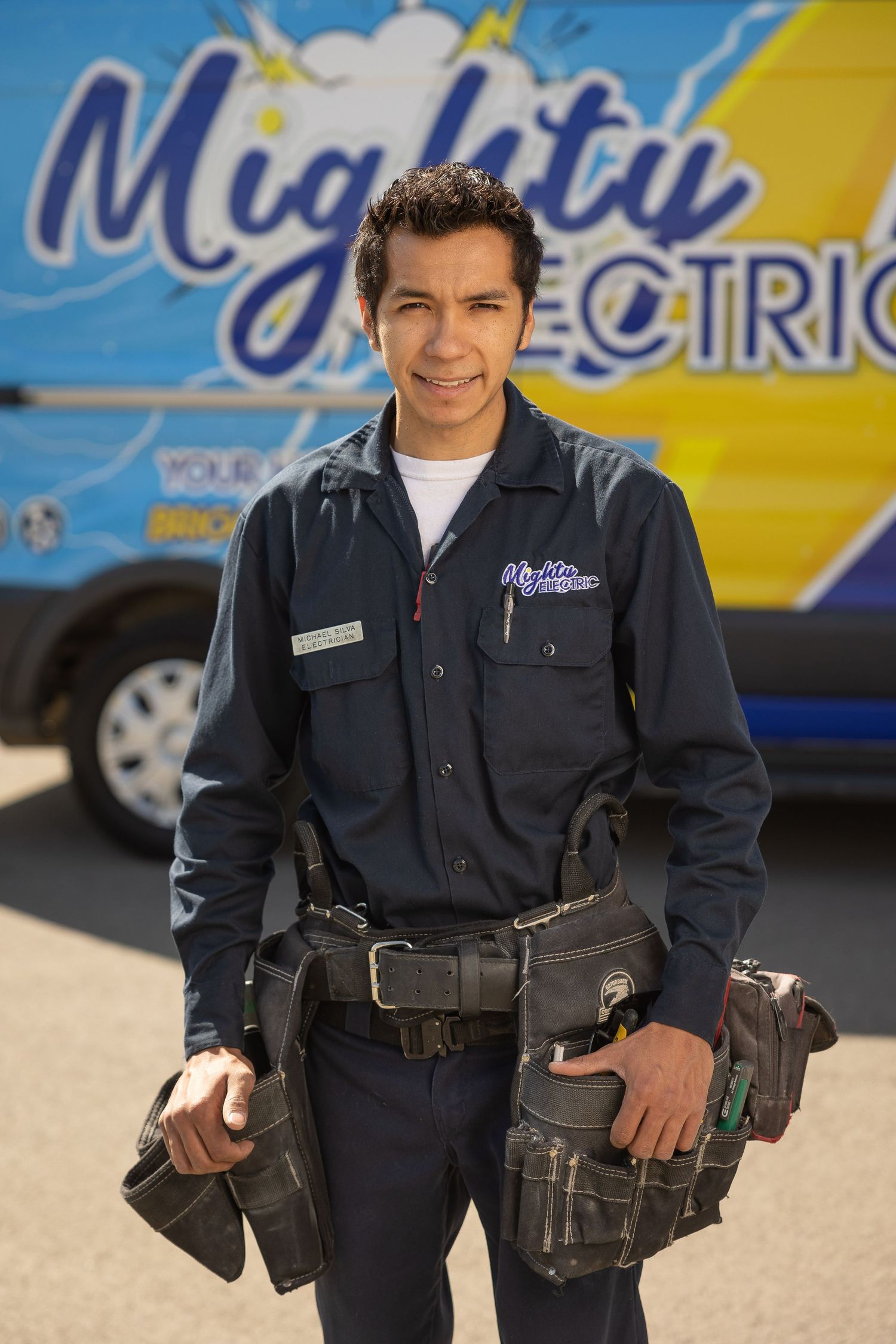 Professional technician in navy blue uniform with tool belt standing next to service vehicles.