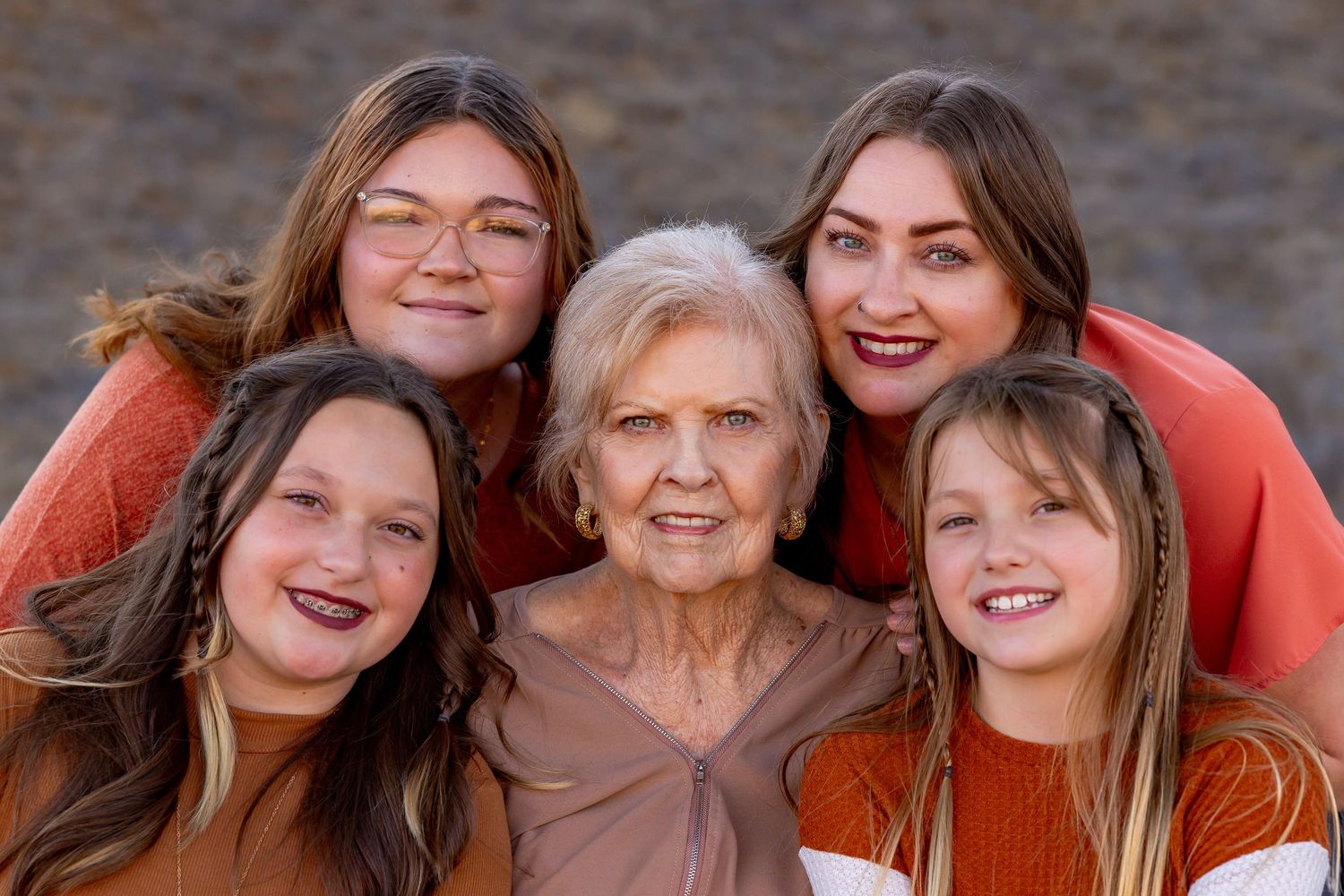 Close-up portrait of family members wearing coral and orange tones against natural background.