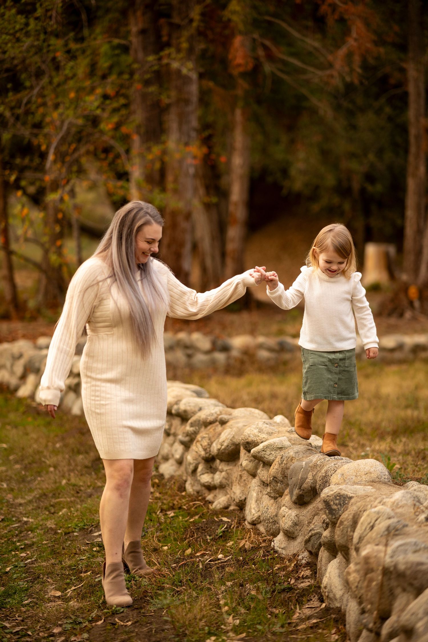 Young child walking along stone wall wearing cream sweater in outdoor autumn setting.