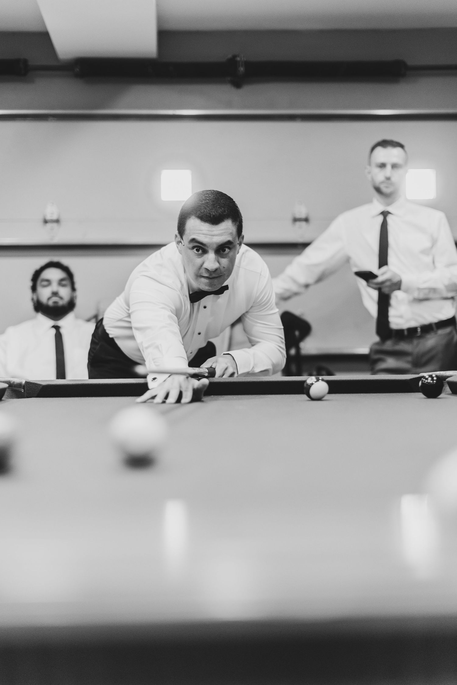 A black and white photo of men playing pool in a casual setting.