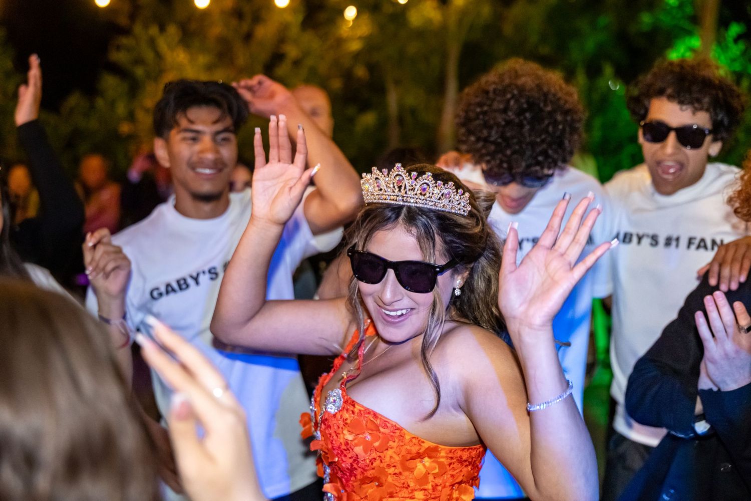 Celebratory dancing scene with people wearing sunglasses and casual attire at an outdoor party.