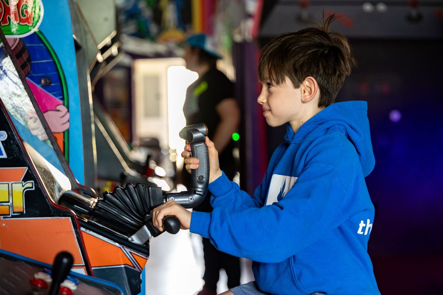 Person wearing bright blue plays arcade games in a colorful gaming environment.