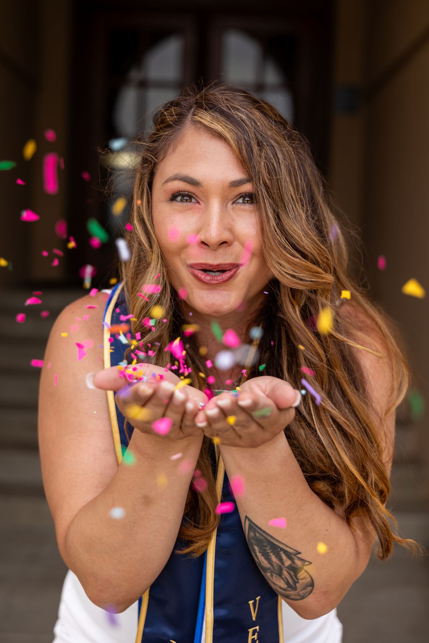 Graduate tossing colorful confetti in celebration under covered walkway in Riverside.