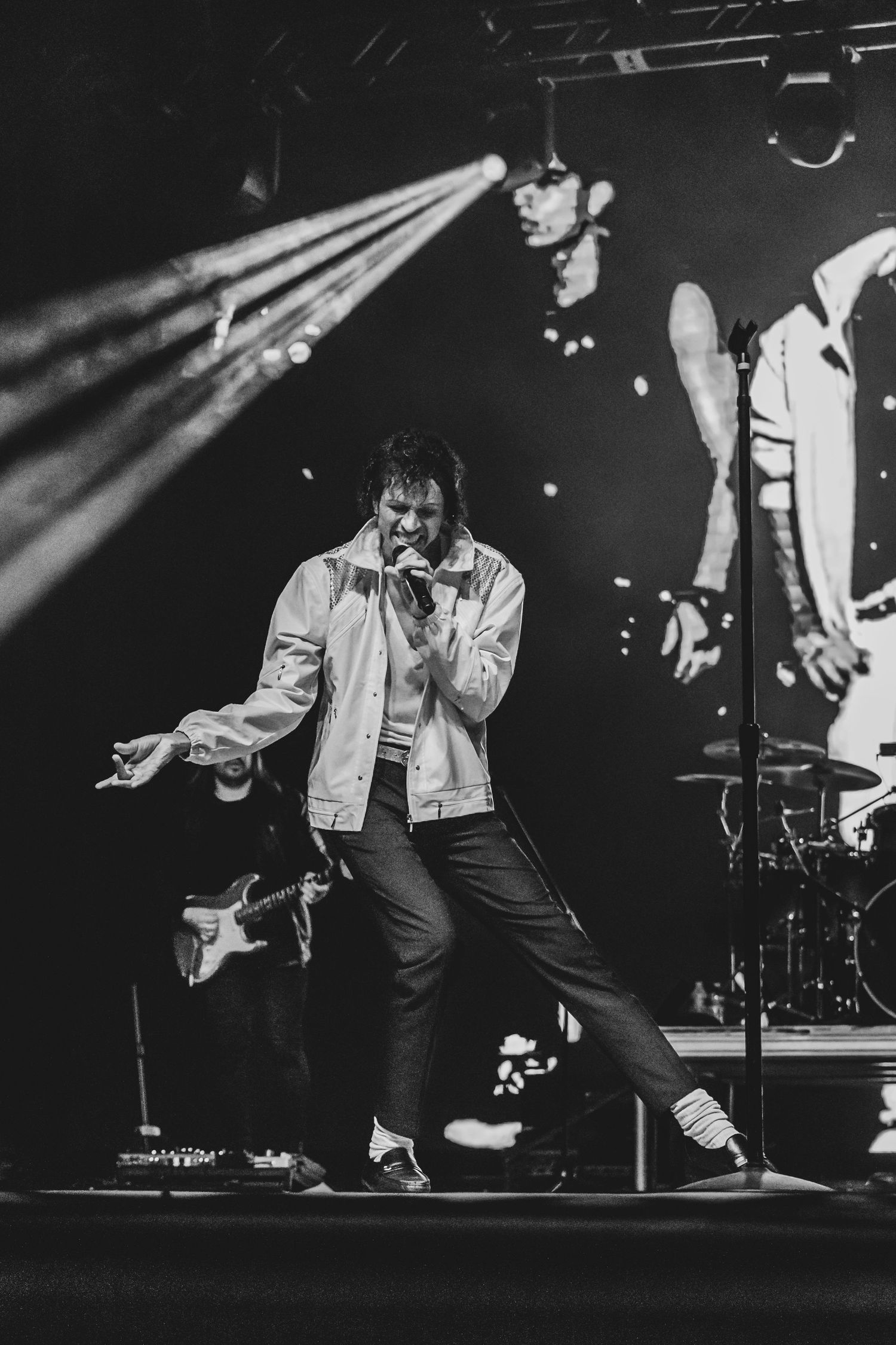 Black and white photo of energetic stage performance with dramatic spotlights.