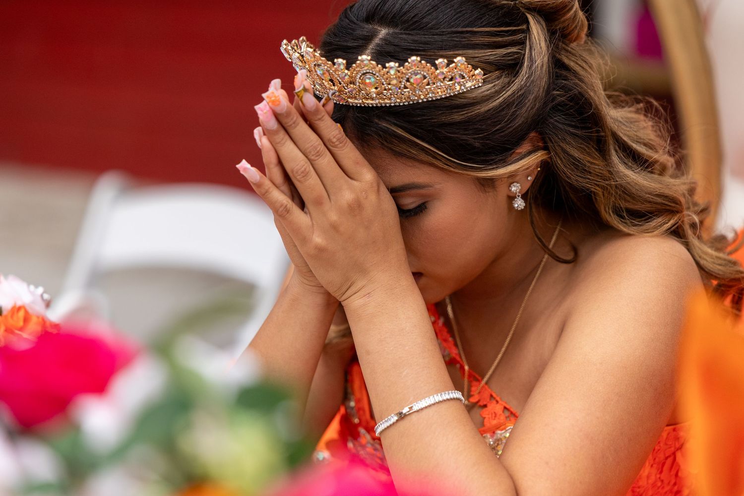 A crown-wearing celebrant in an emotional moment with hands clasped in prayer.