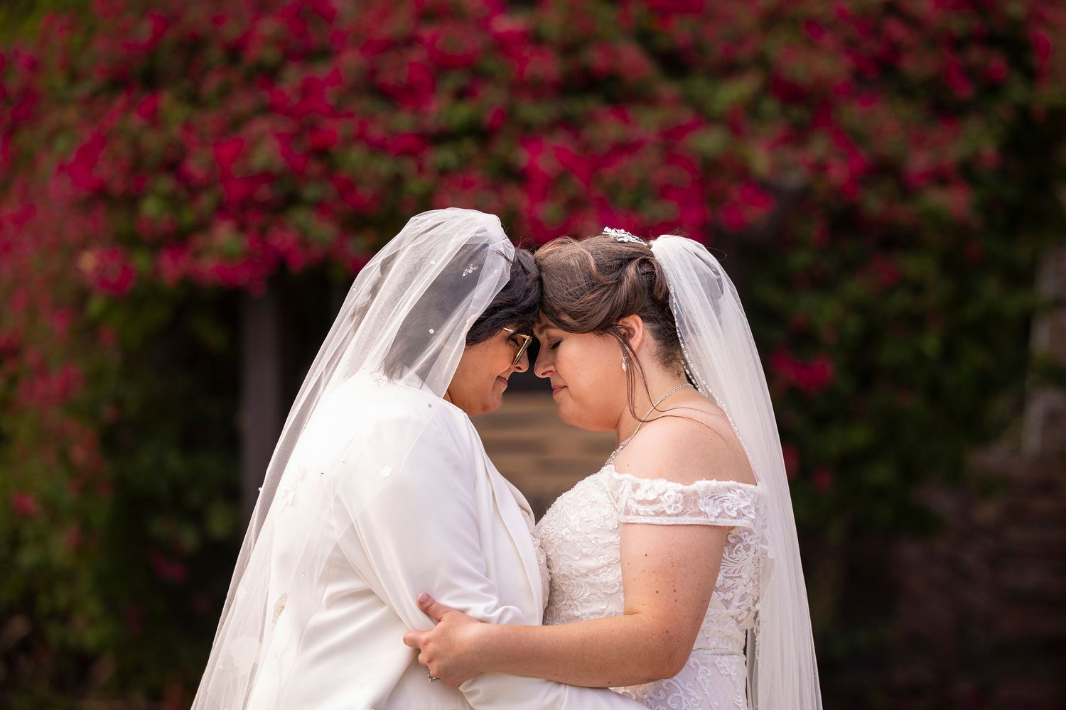 A tender wedding moment captured with vibrant pink bougainvillea flowers in the background.