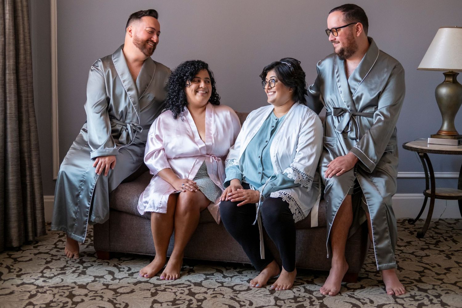 Group in matching robes sit together on a hotel room couch before a wedding ceremony.