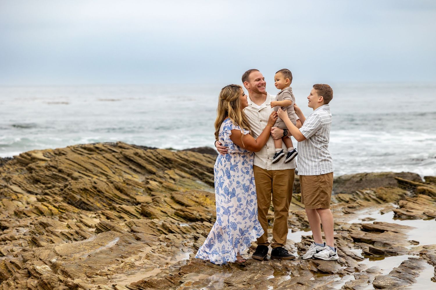 Family sharing joyful moment together on rocky coastal shoreline with ocean waves behind them in Huntington Beach.