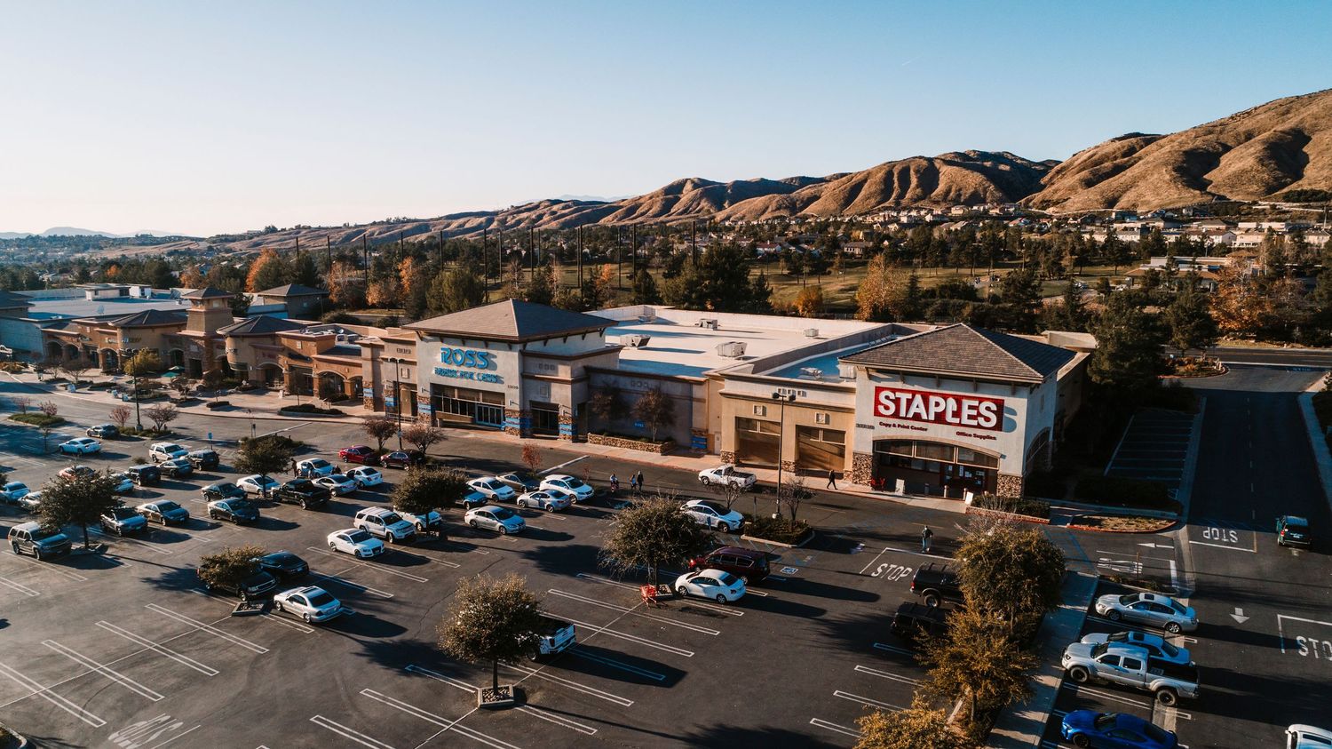 Aerial panoramic view of vast parking lots and commercial buildings with mountains in the background during daytime.