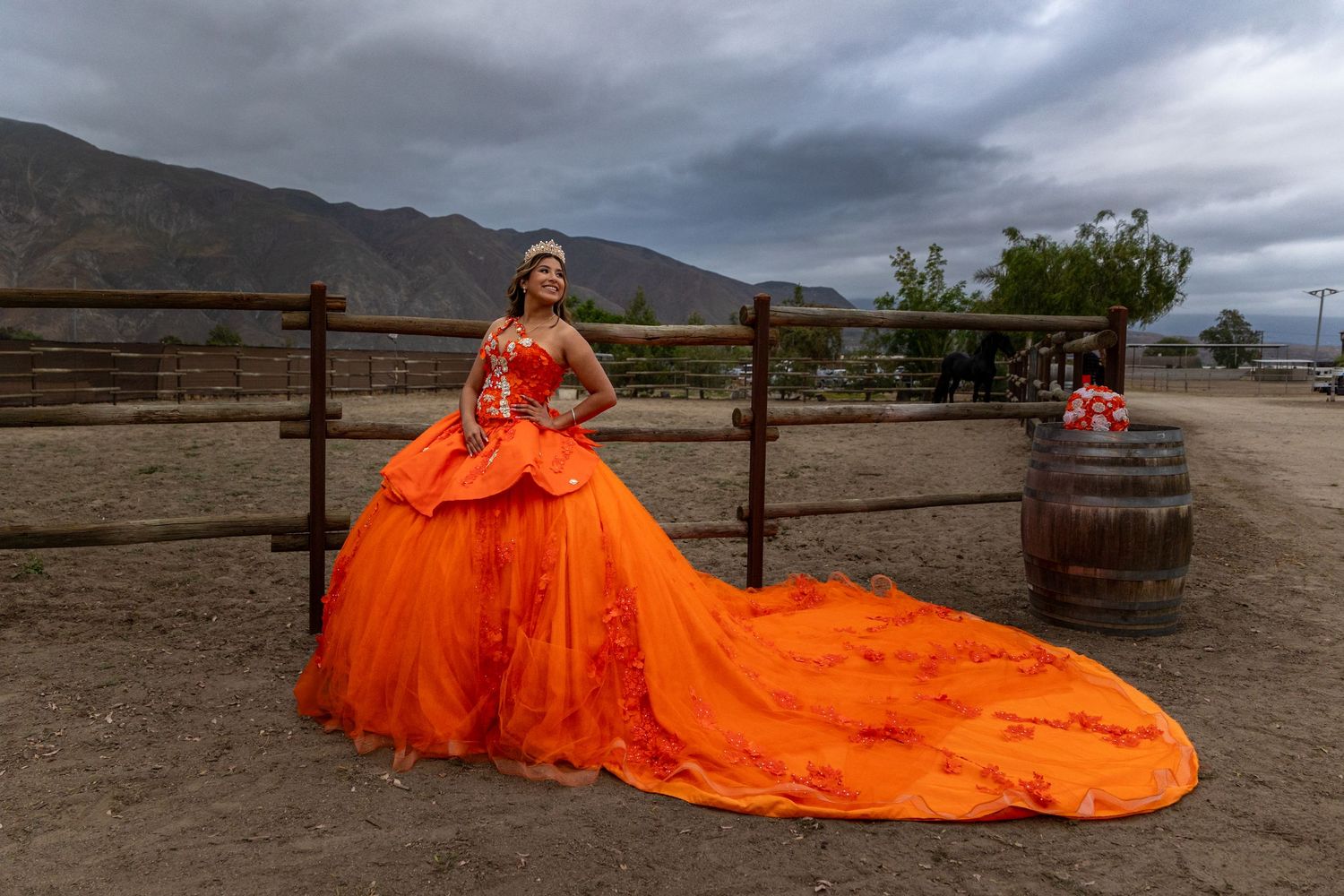 A dramatic orange ball gown with long train photographed against mountains and stormy skies.