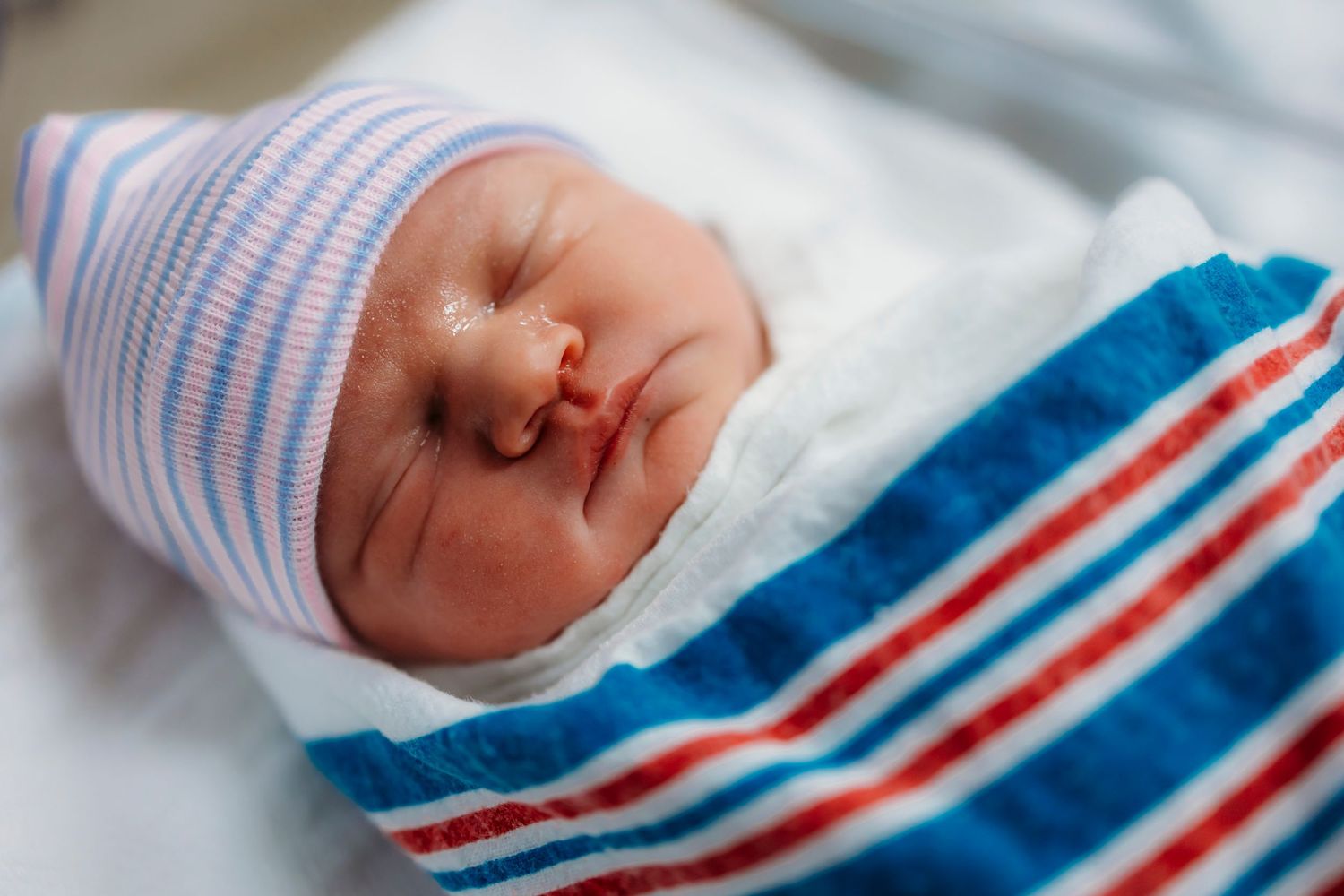 Newborn baby wearing traditional blue and red striped hospital hat.