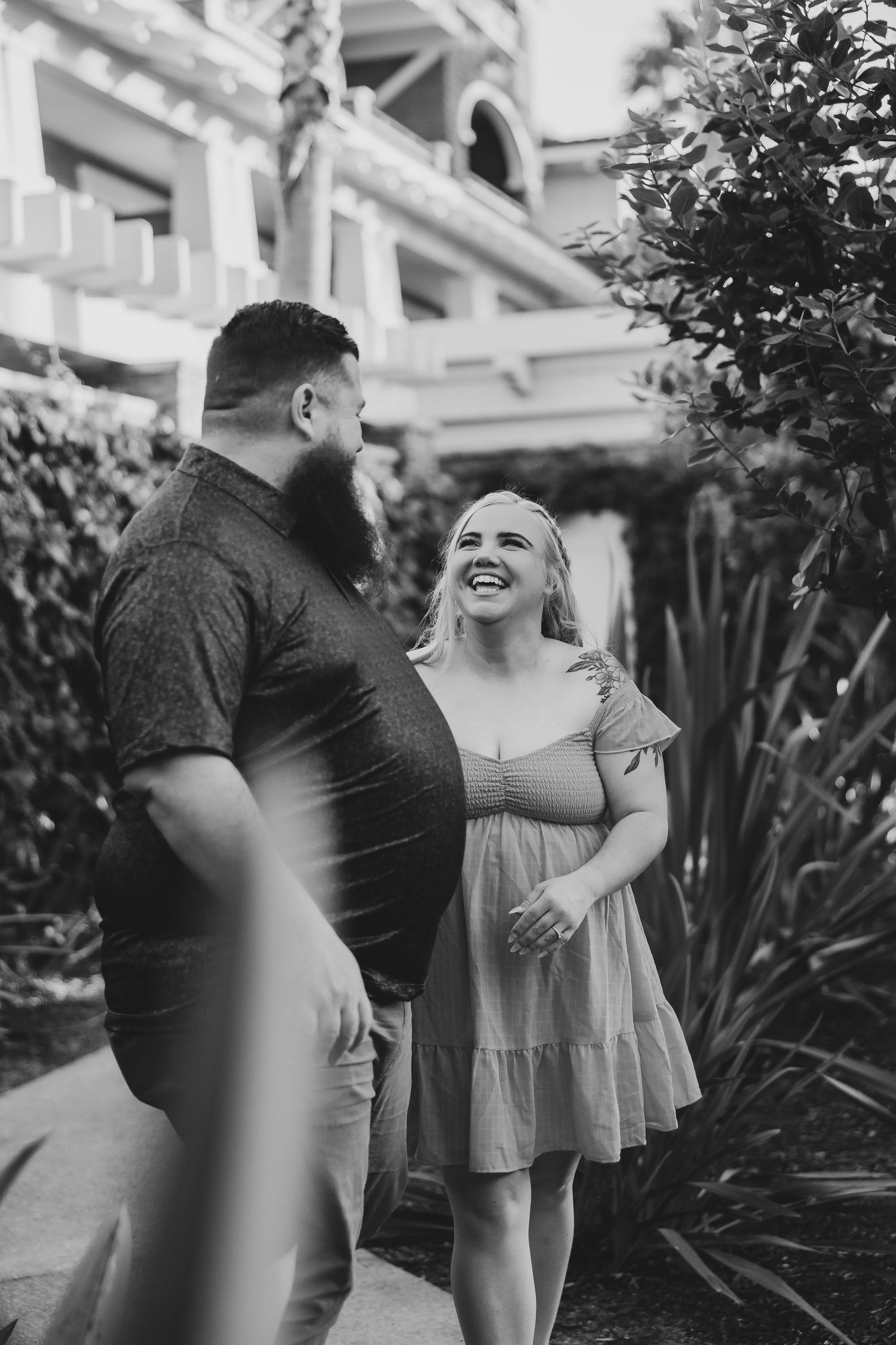 Black and white photo of people sharing a candid moment in front of a white building with tropical plants.