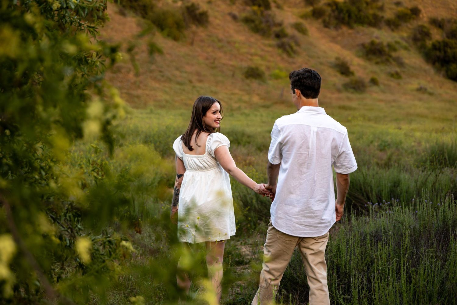 A couple in white outfits walking together through a scenic mountain landscape.