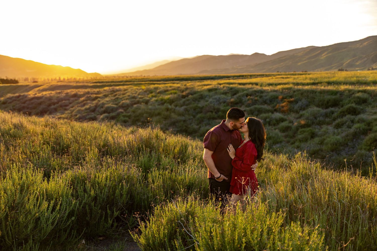 A romantic sunset photoshoot amid tall grasses in a scenic mountain landscape.