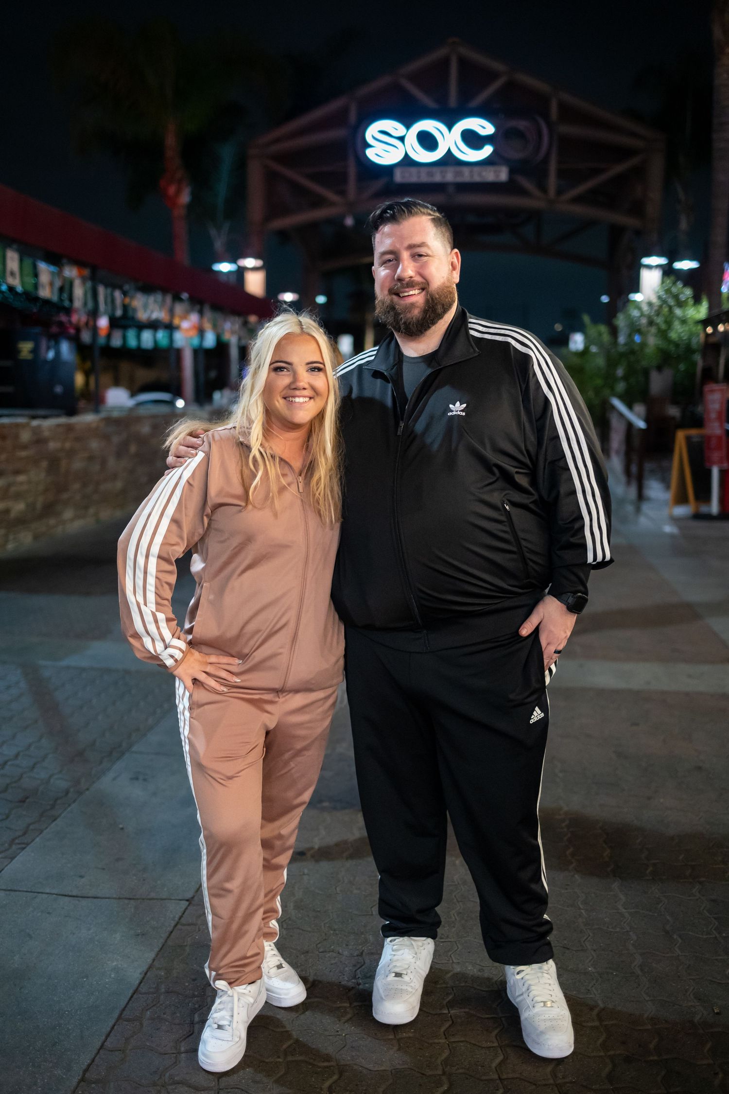 Couple in matching athletic wear posing outside SOC venue at night.