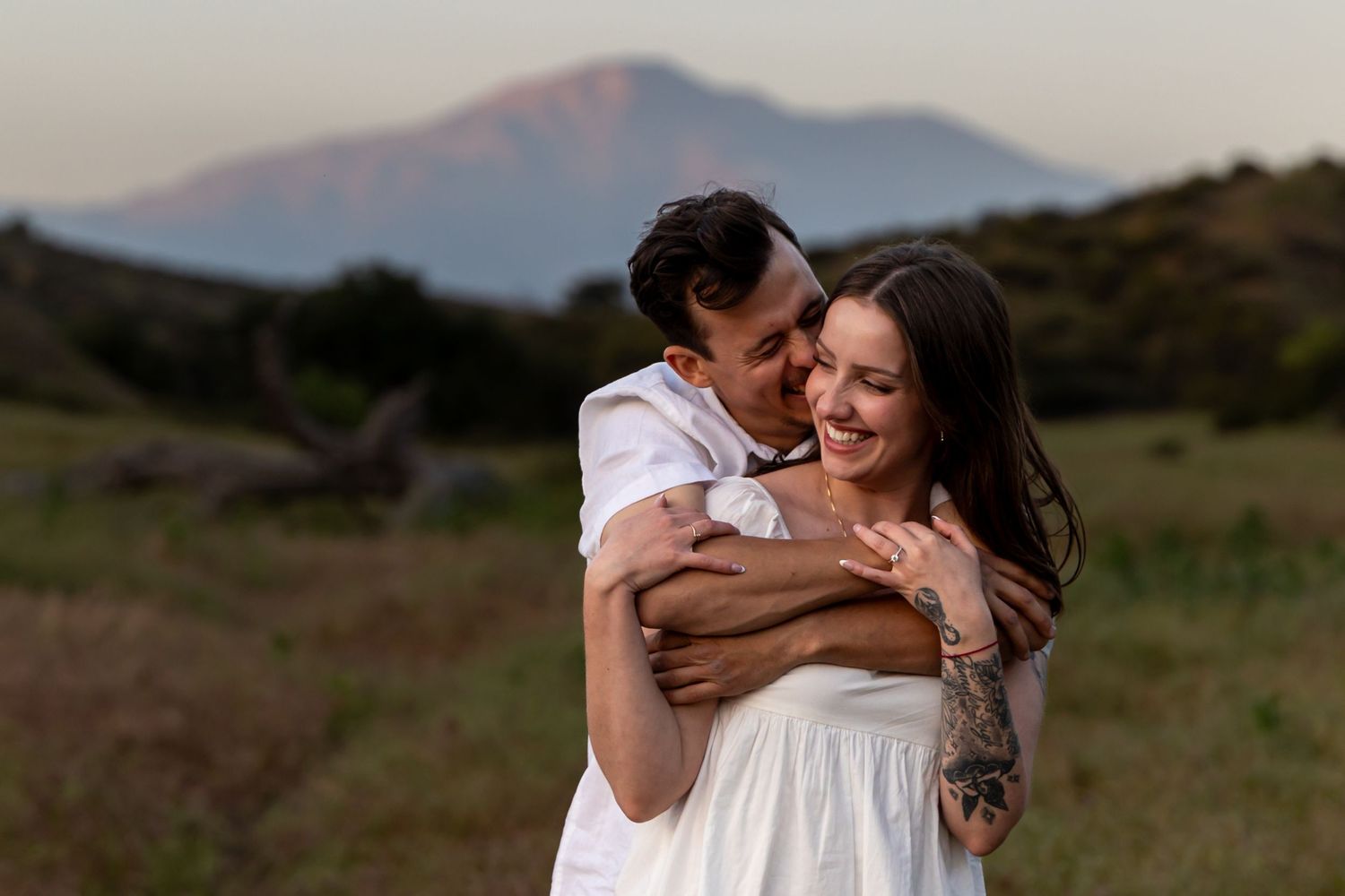 A romantic outdoor embrace captured in a field at sunset with mountains visible in the background in Redlands.