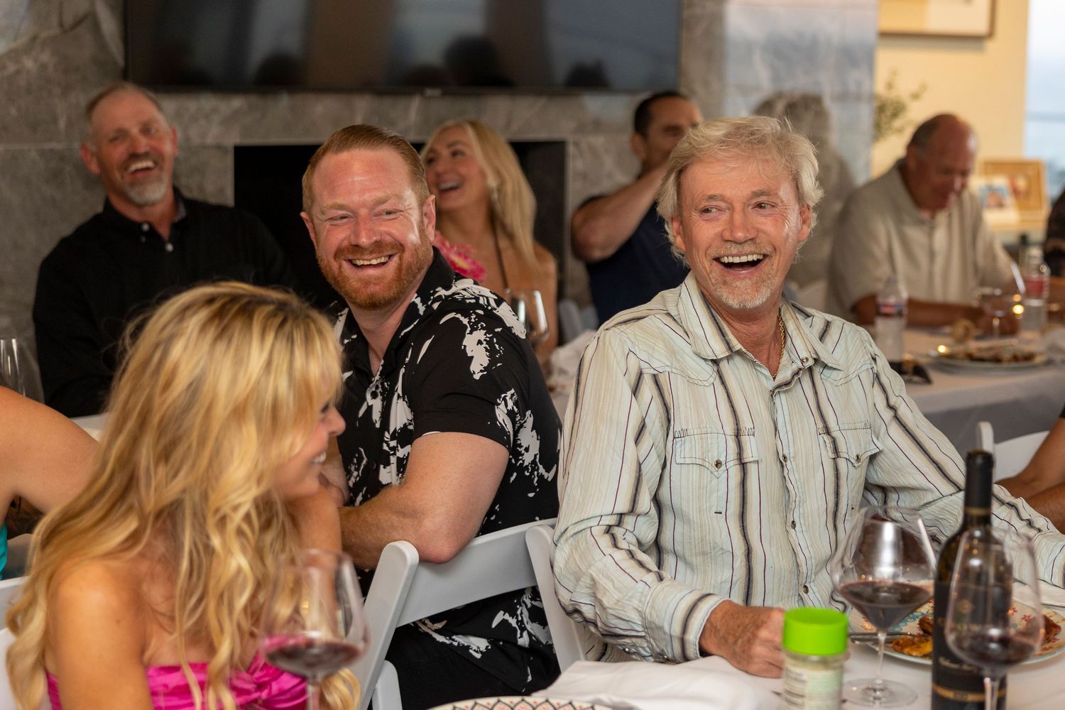 Guests laughing and socializing around a dining table at an evening event.