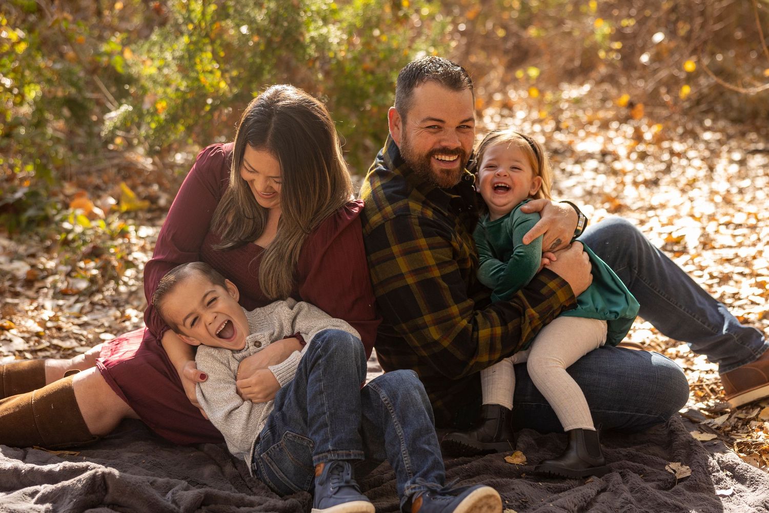 A family lies together on fallen autumn leaves during an outdoor photo session.