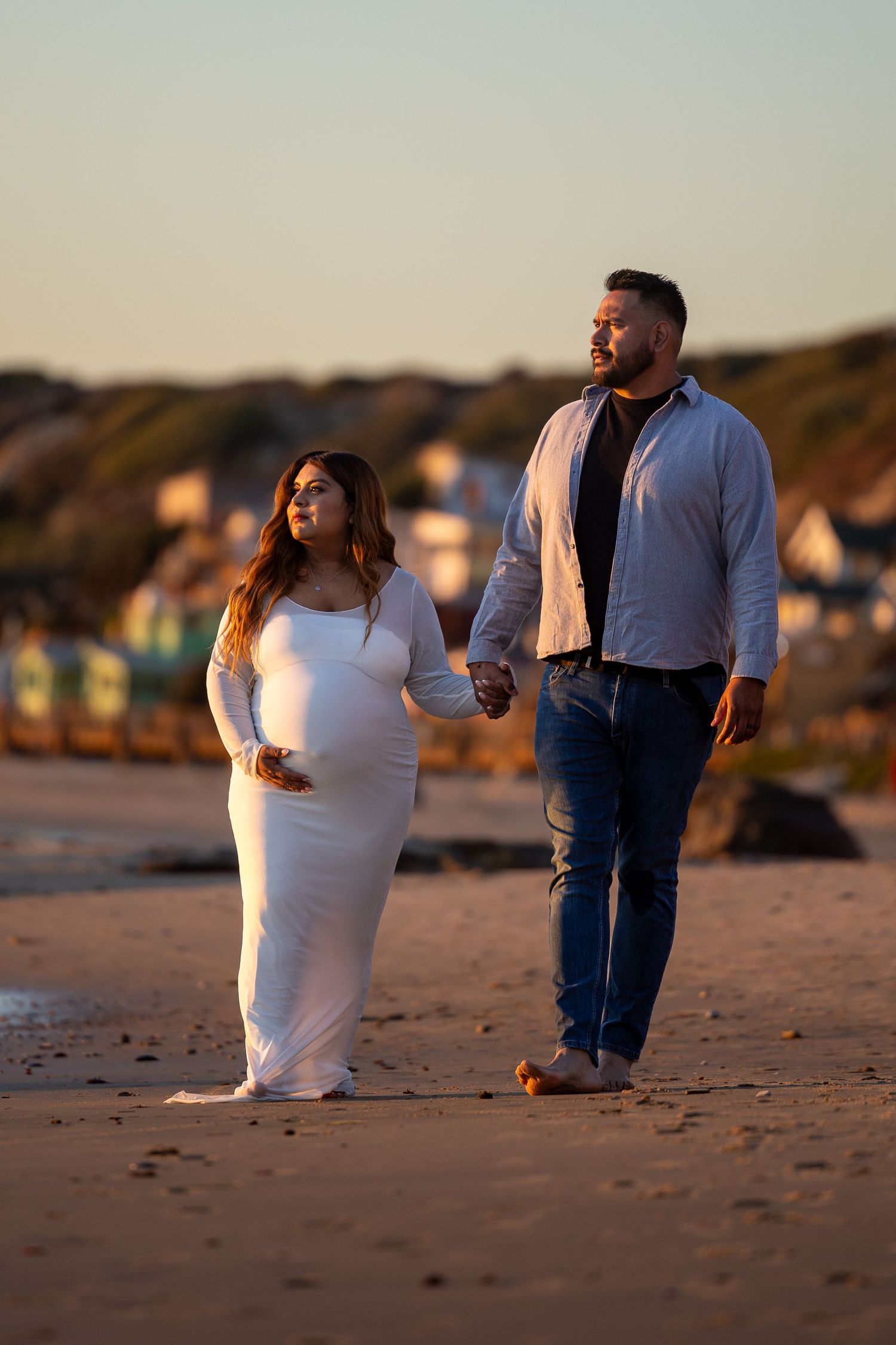 Couple walking along a sandy beach during sunset with soft golden lighting.