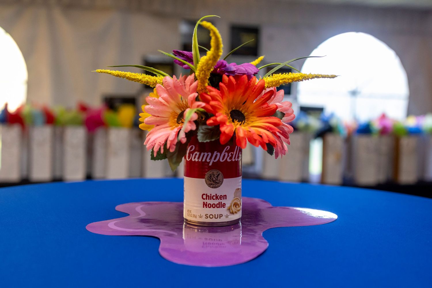 Bright gerbera daisy centerpiece in pink vase on blue tablecloth at event.