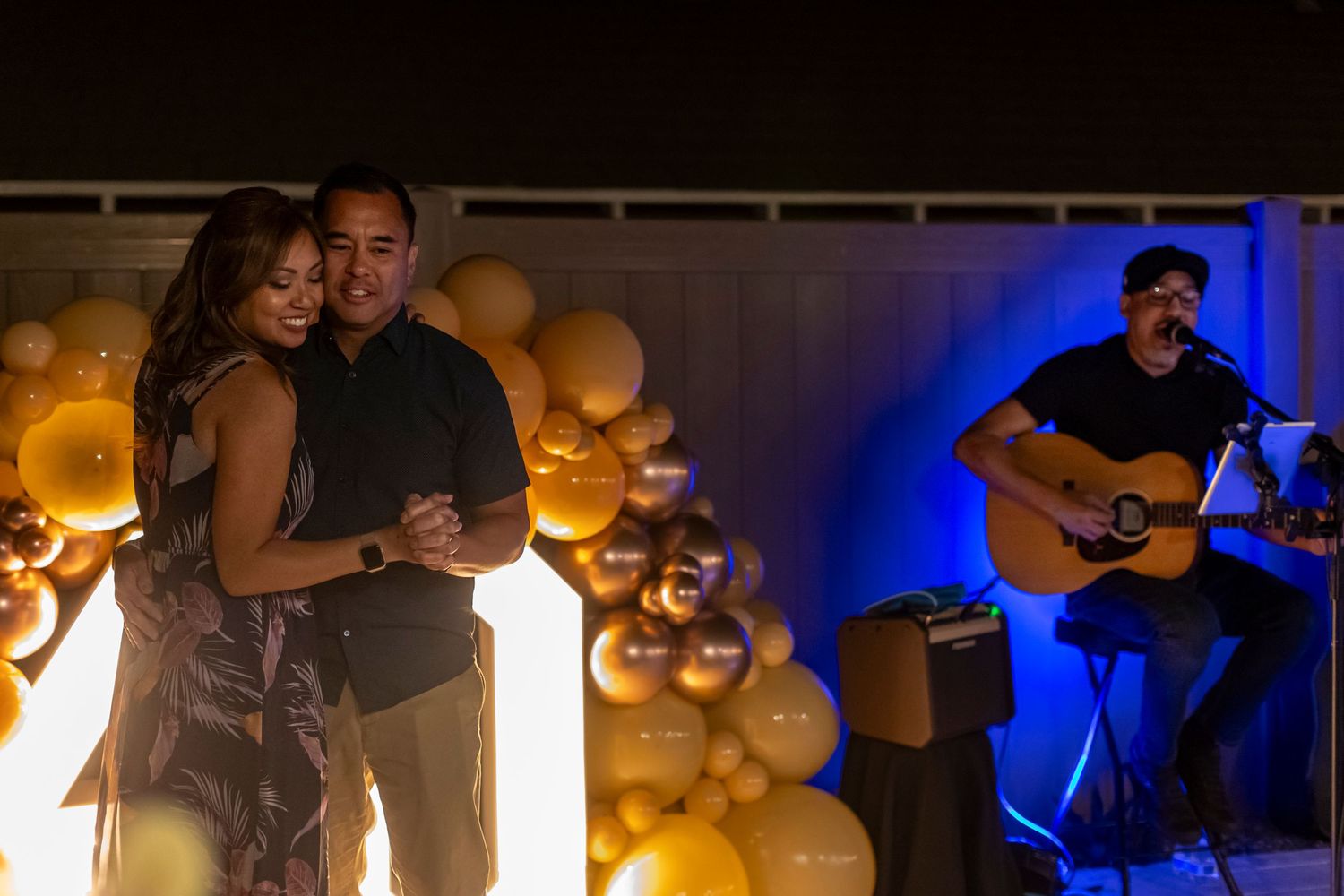 Couple dancing while musician performs with acoustic guitar against balloon backdrop with blue lighting in Anaheim.