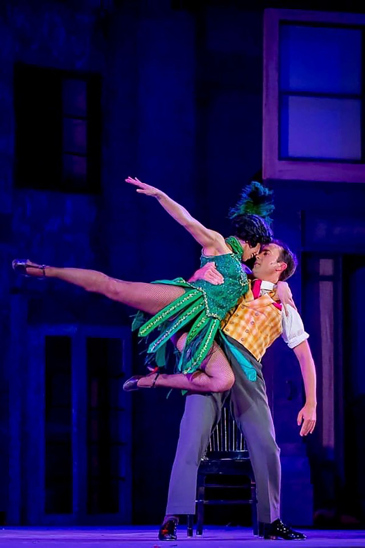 Dancers performing a dramatic lift in colorful costumes during theatrical stage production.