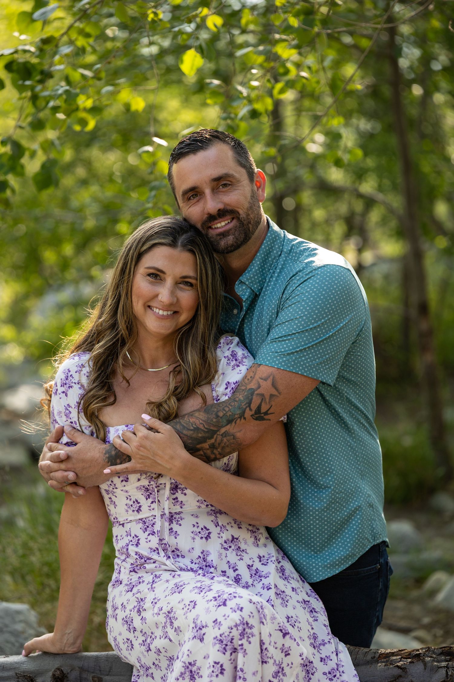 A couple embraces lovingly in a romantic outdoor photoshoot surrounded by lush greenery.