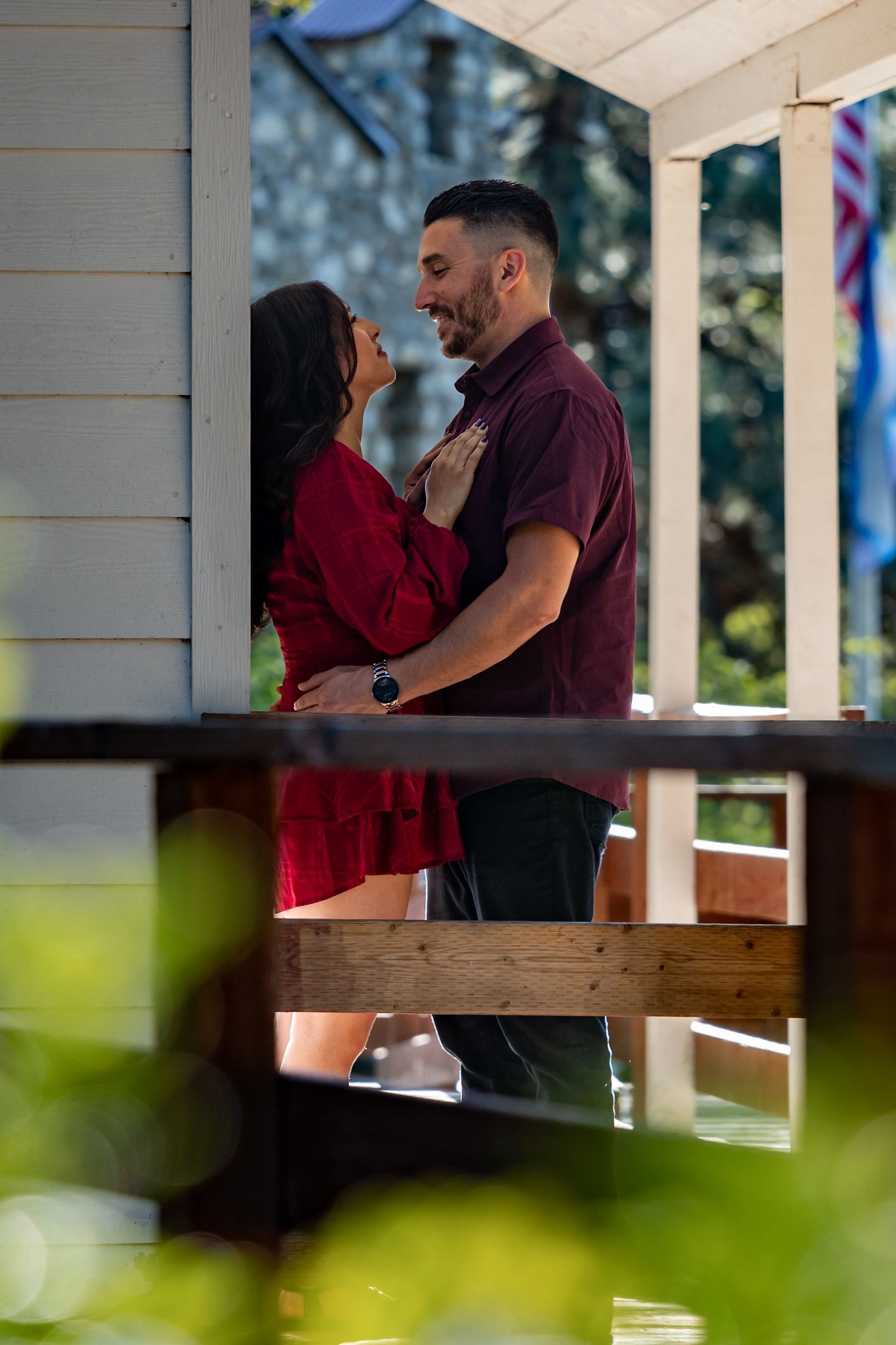 A romantic moment shared between a couple on a porch in burgundy clothing.