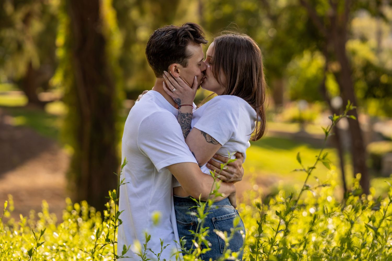 A romantic couple embraces in a beautiful spring meadow filled with yellow wildflowers and sunlit trees in Redlands.
