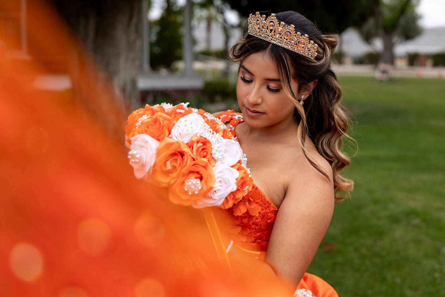 Quinceañera in orange gown with floral bouquet poses in outdoor setting in San Jacinto.