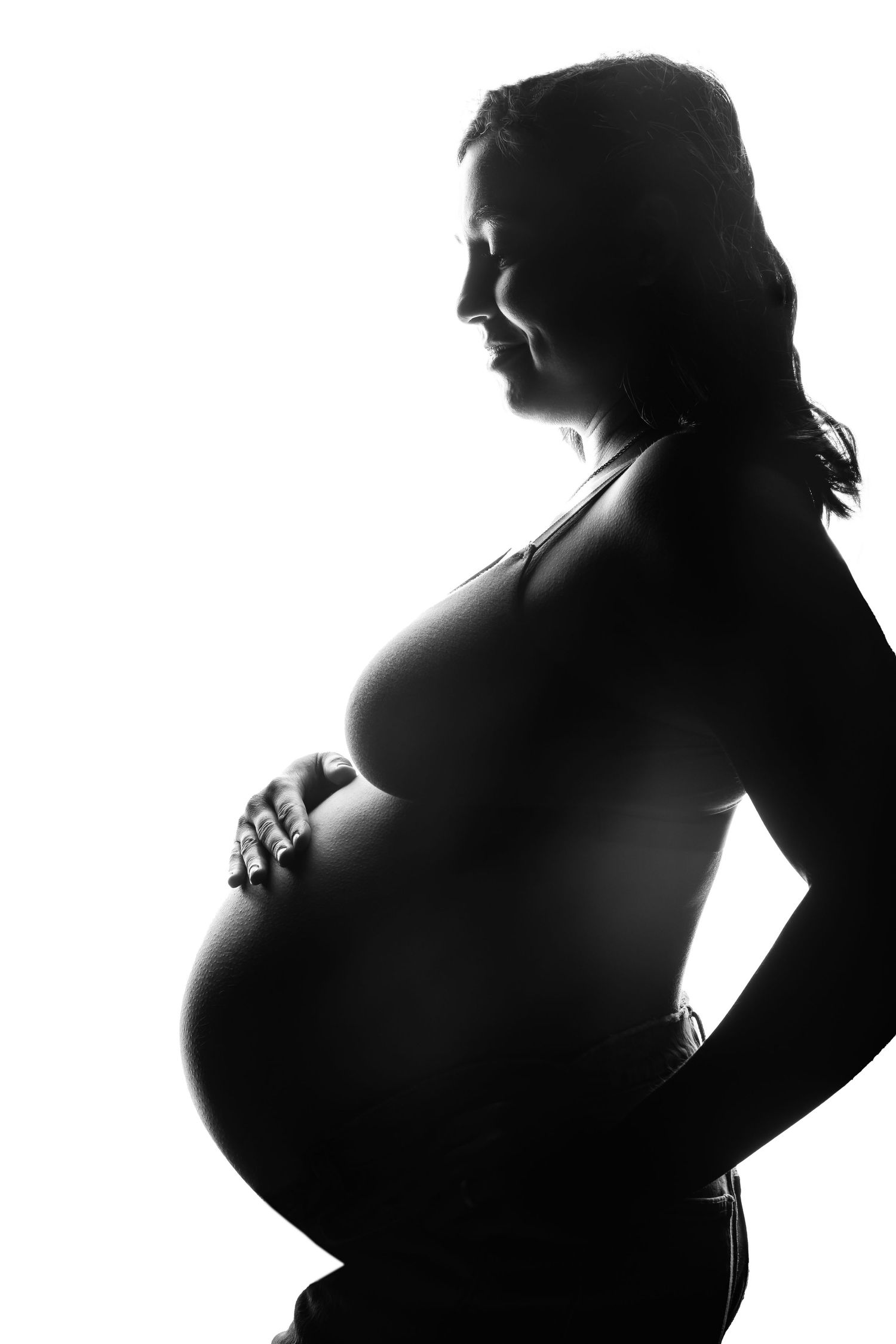 Black and white silhouette of pregnant woman standing sideways showing her baby bump taken on location in Laguna Beach.