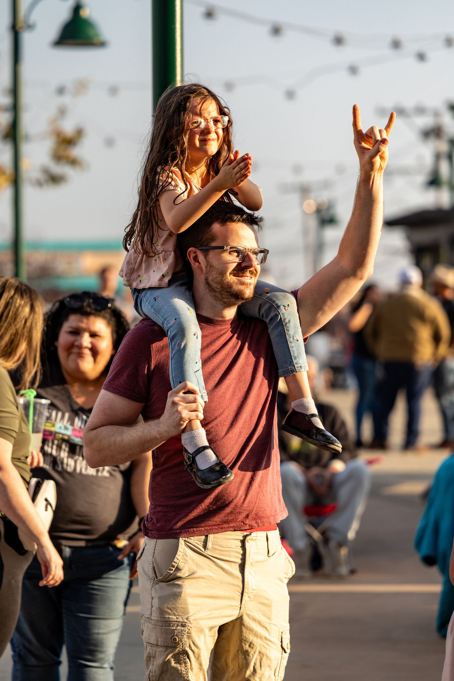 Festive crowd enjoying an outdoor concert at sunset with people making rock hand gestures.