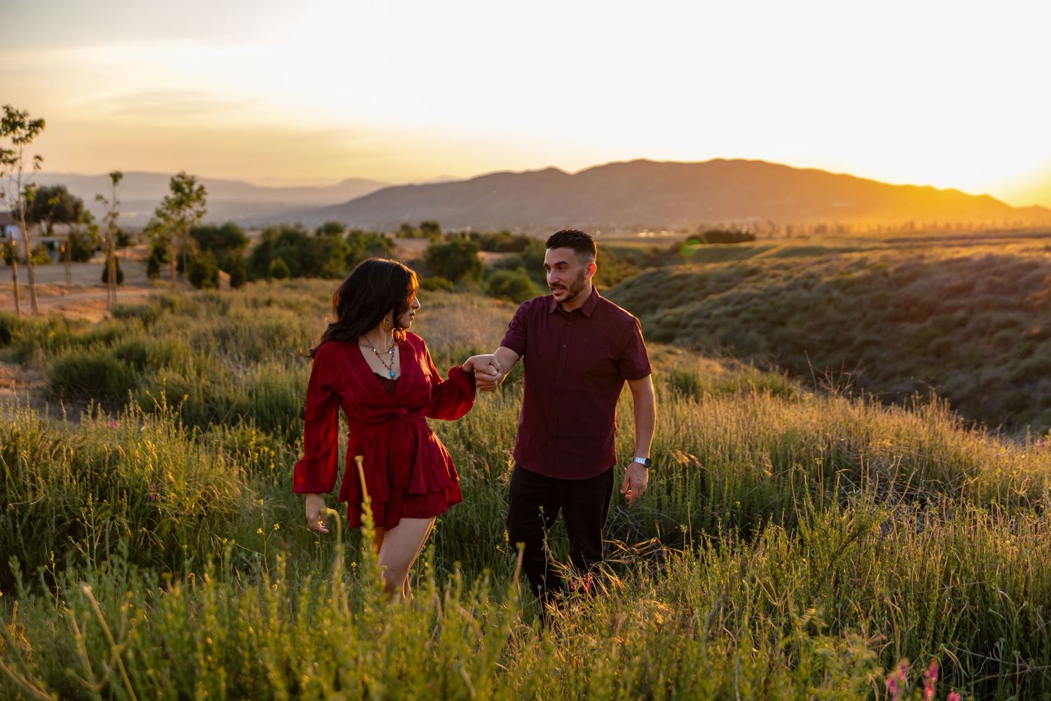Couple walking through tall grass in a mountain field during sunset.