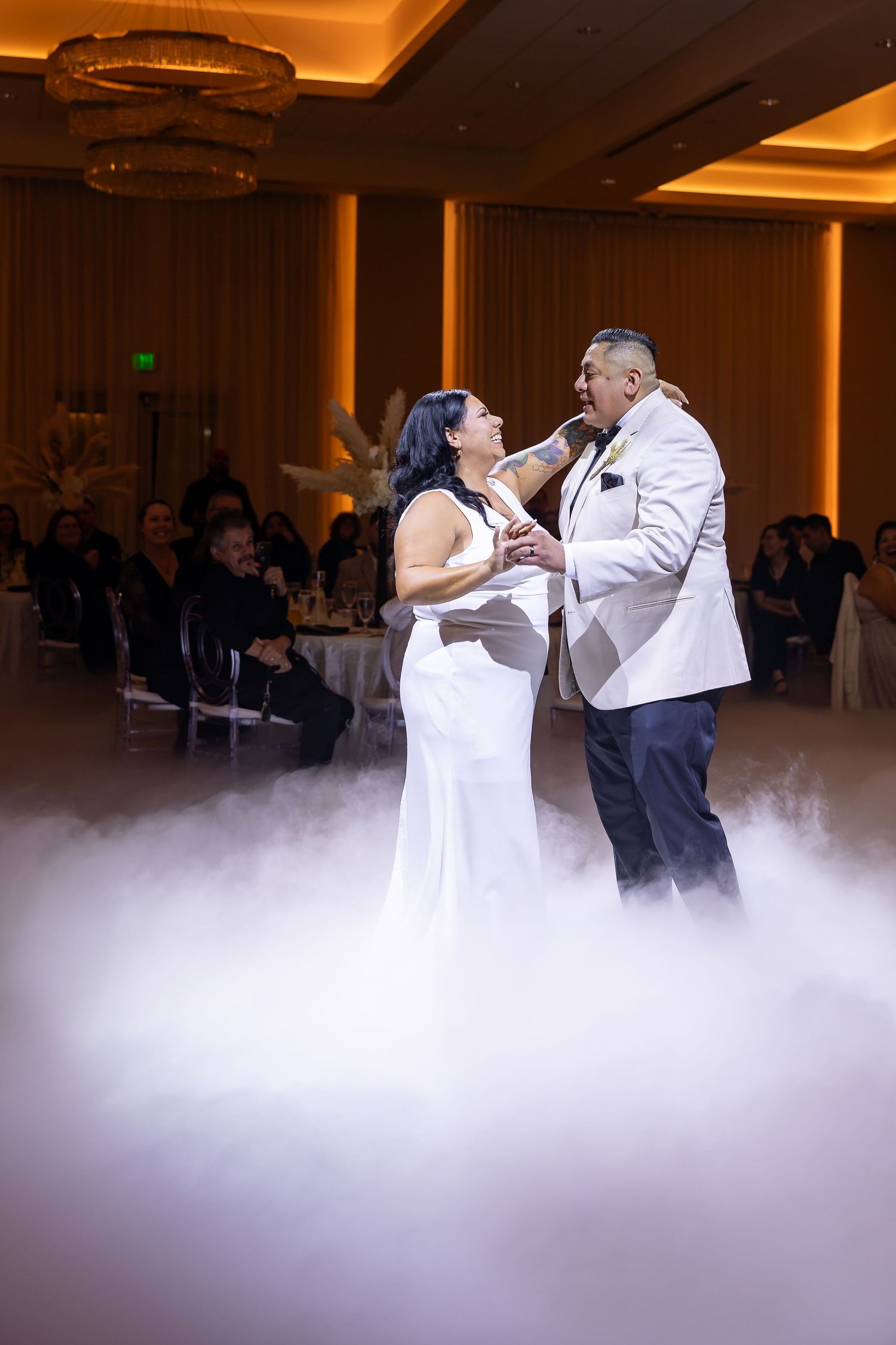 A couple shares a romantic first dance amidst dramatic fog effects on their wedding dance floor.