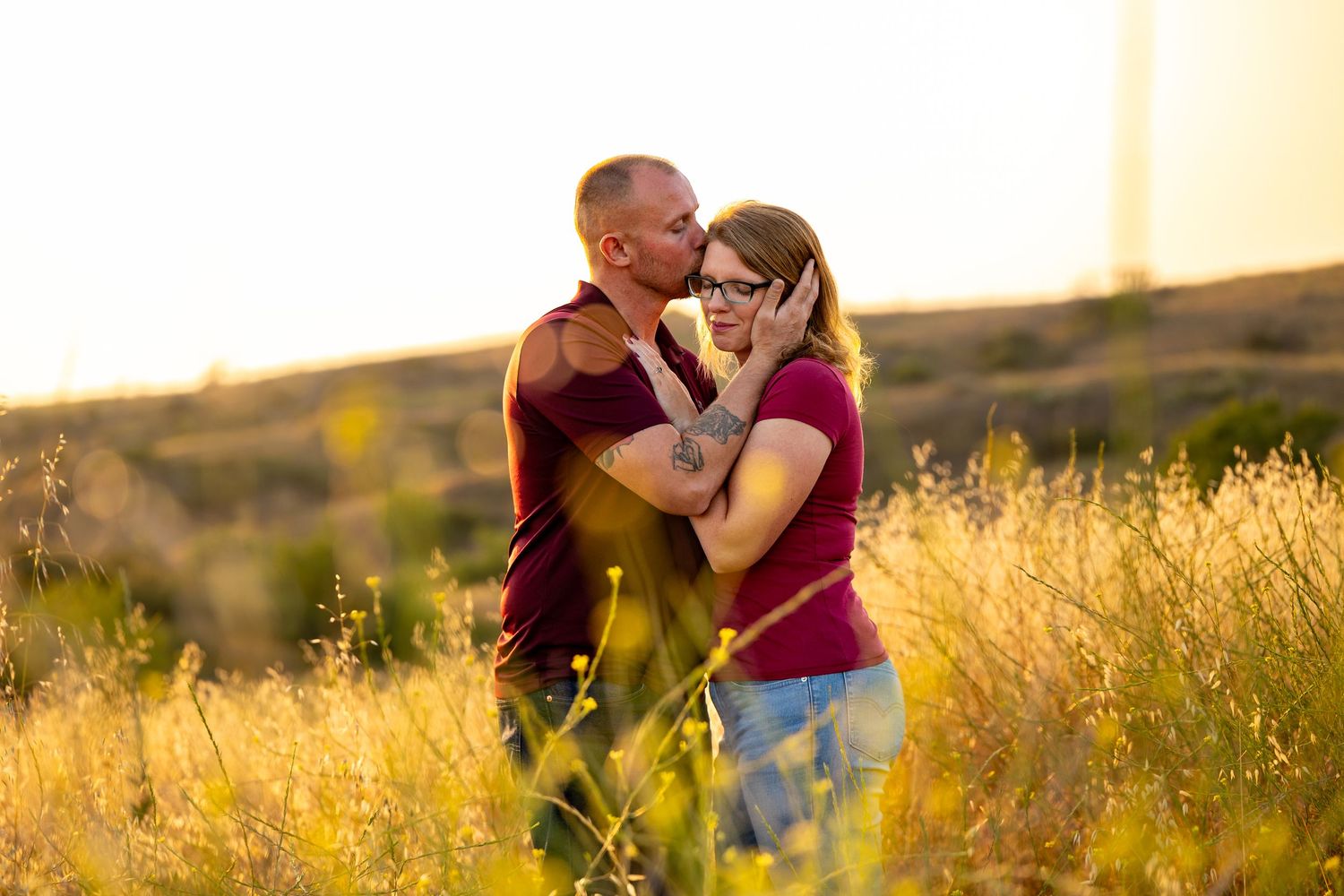 A couple embraces in a sunlit field of golden grass at sunset.
